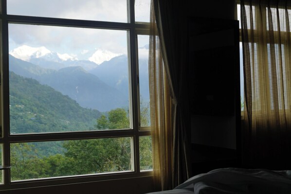 A room with a large window offering a view of snow-capped mountains and lush green hills.
