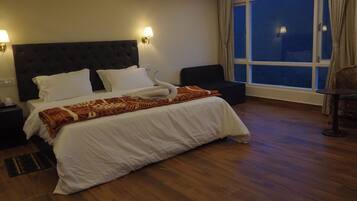 Una habitación de hotel con una cama grande, dos lámparas de noche, una silla y un ventanal con cortinas.