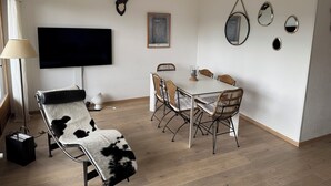 En moderne stue med et fladskærms-tv, en lænestol i kohide, et spisebord med fletstole, et monteret hjorteskjæl og minimalistisk vægdekoration.