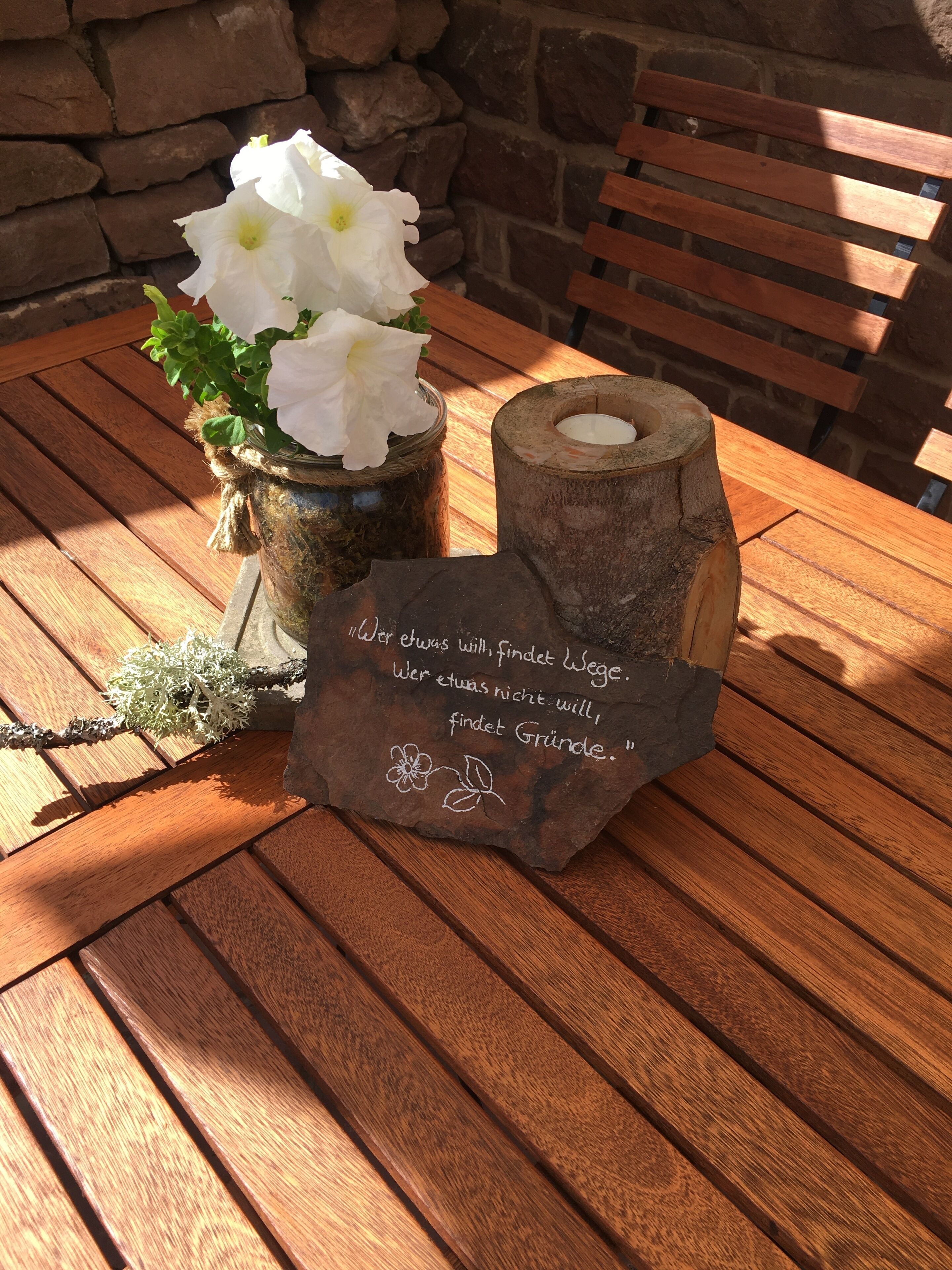 A wooden table with a stone candle holder and a vase of white flowers.