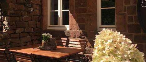 A patio area with a wooden table and benches, a stone wall, and a window with a view.