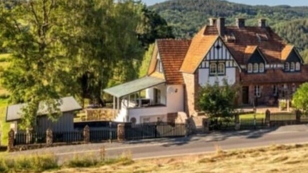 Eine Reihe traditioneller Fachwerkhäuser mit Satteldächern, eine gepflasterte Straße davor und eine hügelige Landschaft im Hintergrund.