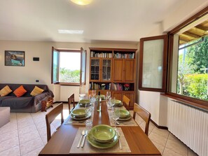A dining area with a wooden table set for six, flanked by a sofa and a bookshelf. - D1MORA Fiorita - Villa with Lake View and Garden (Salò)