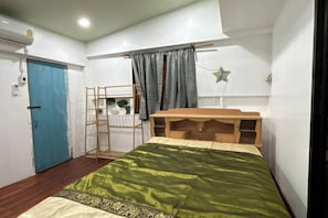 Um quarto pequeno e bem iluminado, com uma cama, uma escrivaninha, uma escada e uma porta azul.