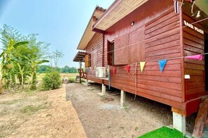 Una casa de madera con porche, rodeada de follaje y un sendero de tierra.
