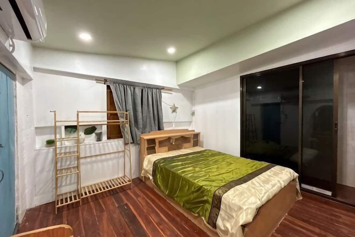 Een slaapkamer met een bed, een houten ladder, een bureau, een stoel, een raam met gordijnen en een schuifpui.