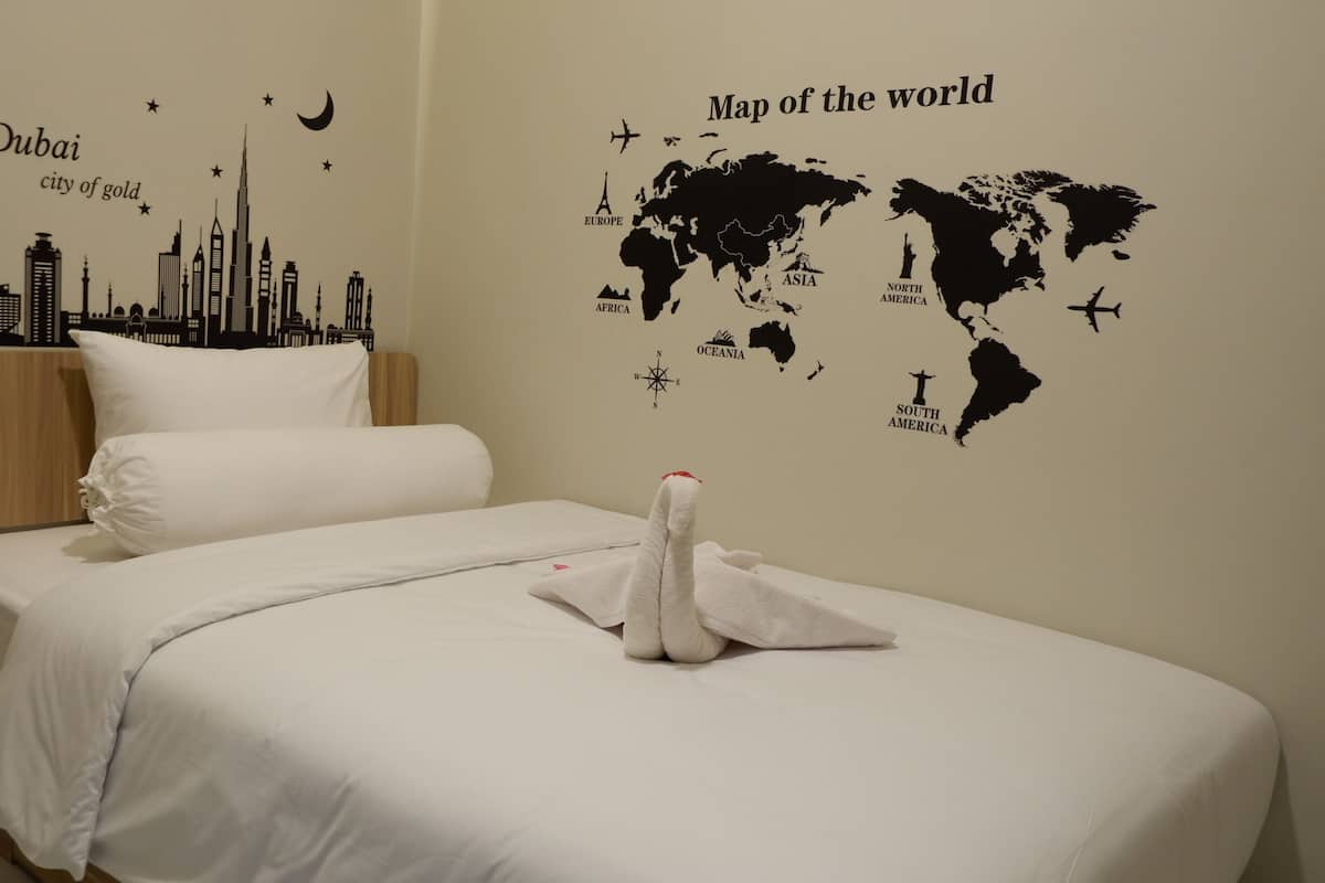 Habitació d'hotel amb un llit, roba de llit blanca, un vinil mural de mapa del món i un vinil mural del skyline de Dubai.