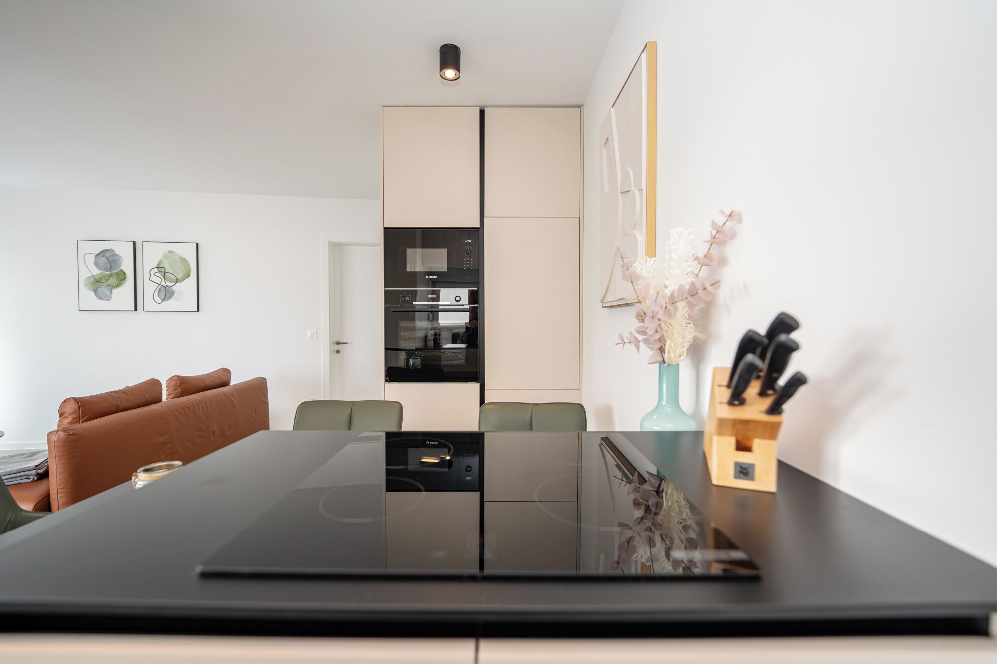 A modern kitchen with a black countertop, a built-in oven, and a dining area with a table and chairs.