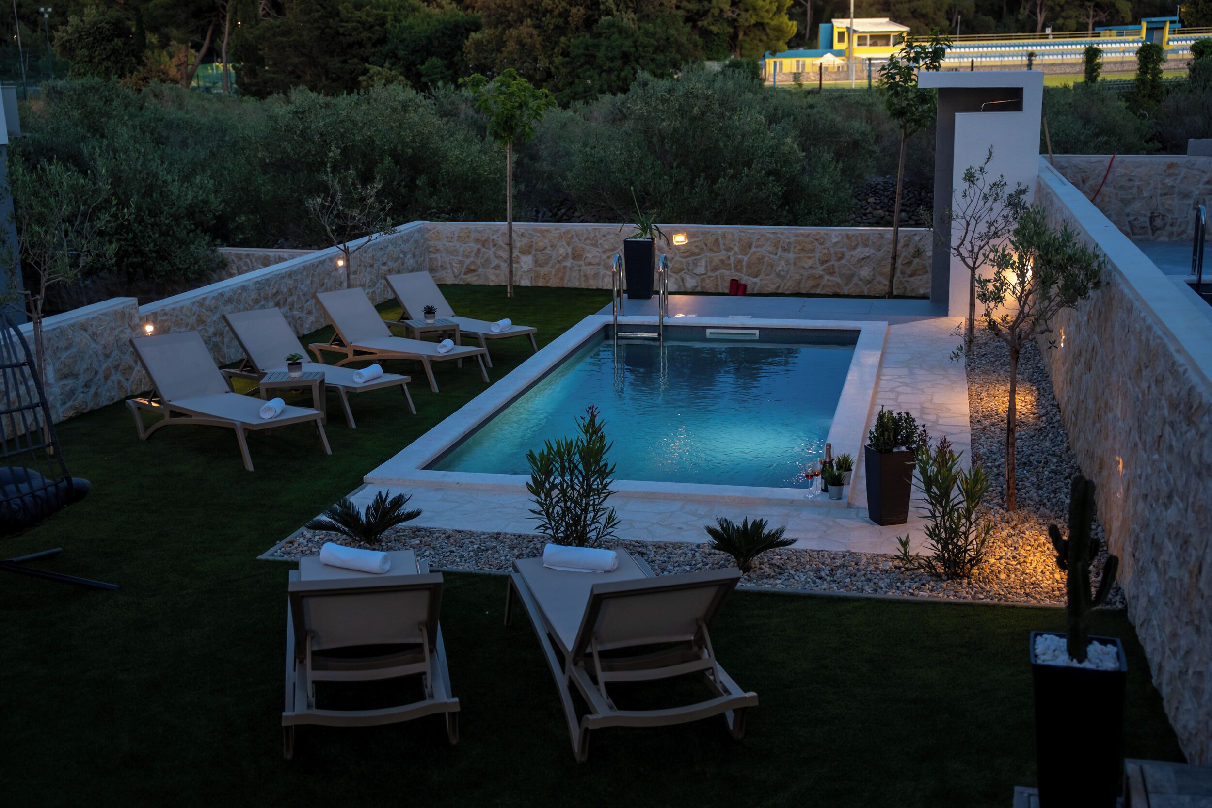A rectangular swimming pool with a stone border, surrounded by lounge chairs and small potted plants.
