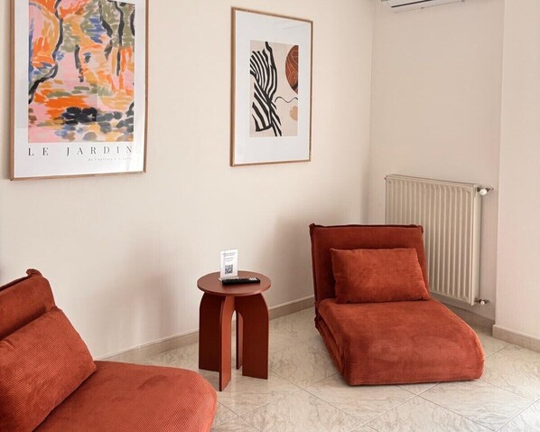 A hotel room with a red sofa, a smaller red chair, a small table with a sign, and two framed artworks on the wall. - Cruise Stop Guest House by Be Your Home (Civitavecchia)