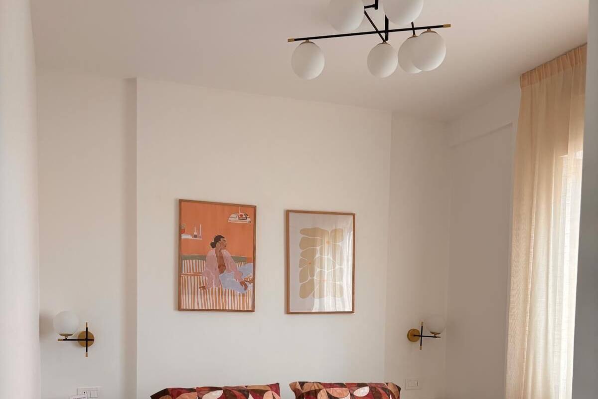 Een hotelkamer met een bed, een nachtkastje, een wandlamp en twee kunstwerken in lijsten.