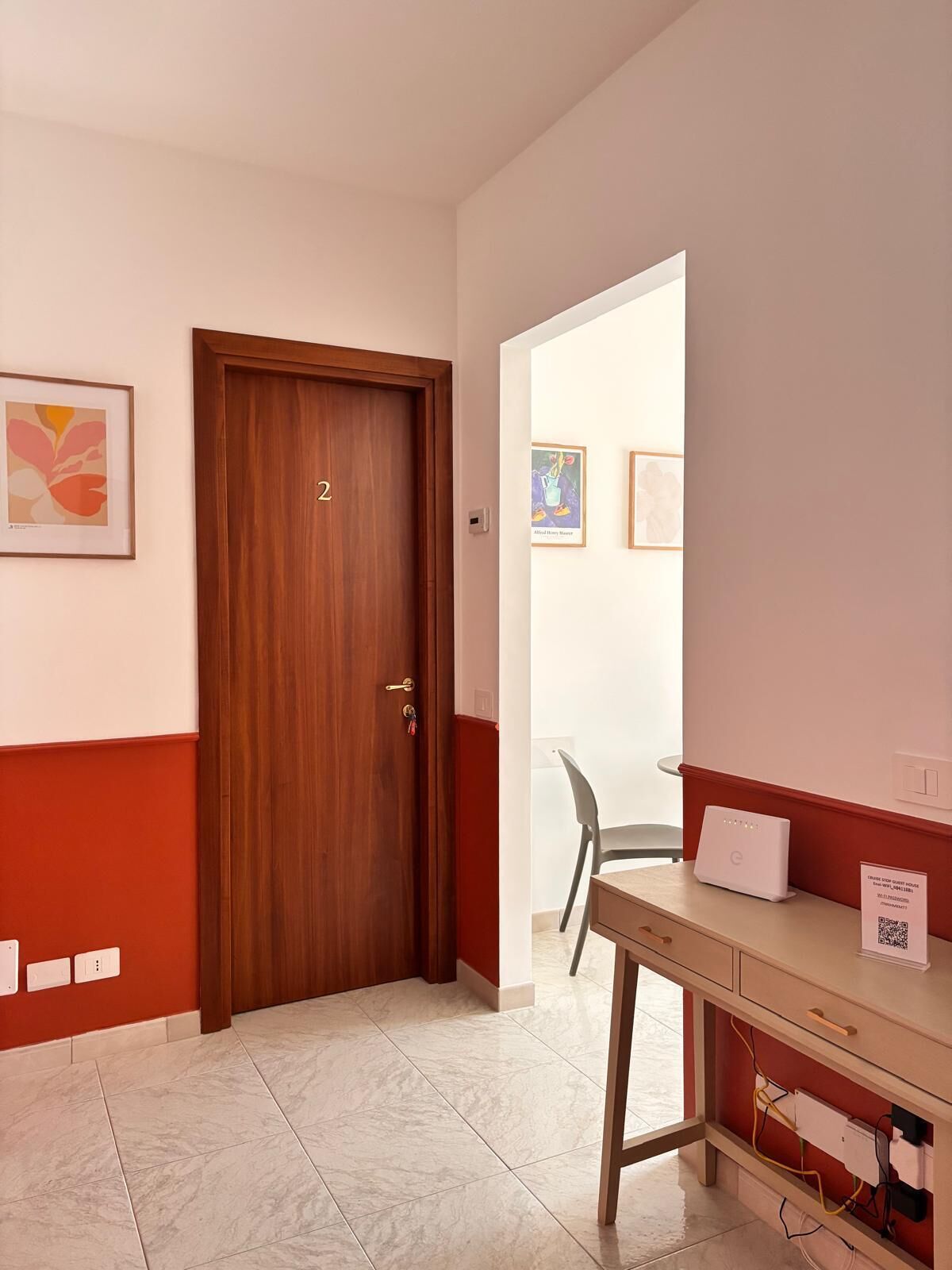 Une chambre d’hôtel avec une porte en bois, un bureau avec un ordinateur portable et une vue sur le couloir.
