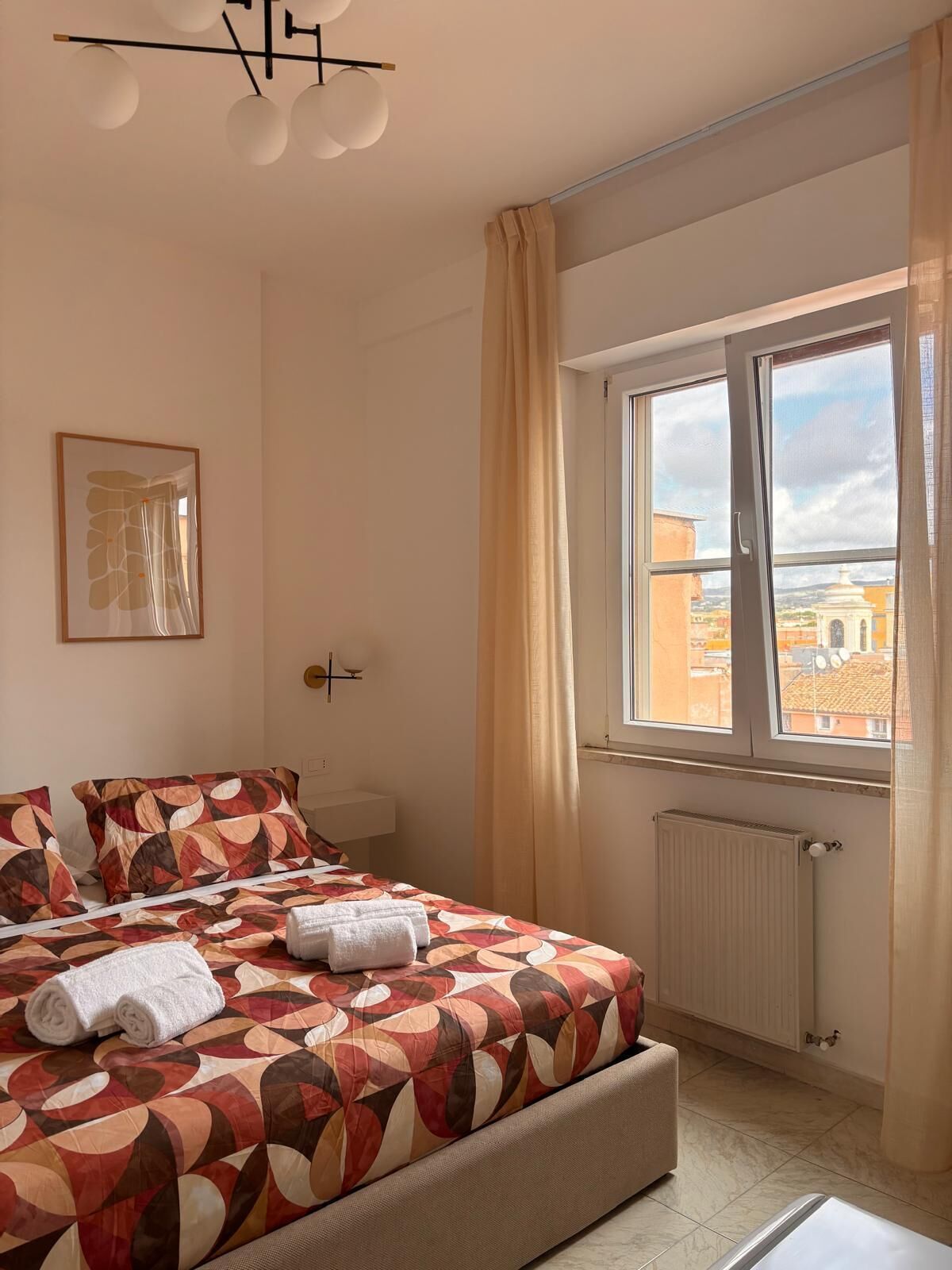 Quarto com cama, janela com cortinas, radiador e luminária no teto.