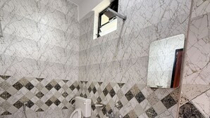 Un baño con inodoro, lavabo y ducha. Las paredes presentan un diseño de mármol con un borde de azulejos tipo diamante.