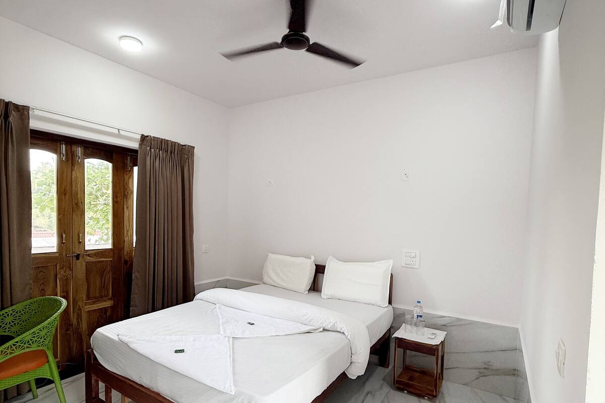 A bedroom with a bed, a wooden nightstand, a green chair, and a ceiling fan.