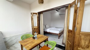 Una habitación con una mesa y sillas de madera, una cama con ropa de cama blanca y un ventilador de techo.