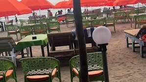 Un área de estar frente a la playa con sillas y mesas verdes, sombrillas rojas y vistas al océano.