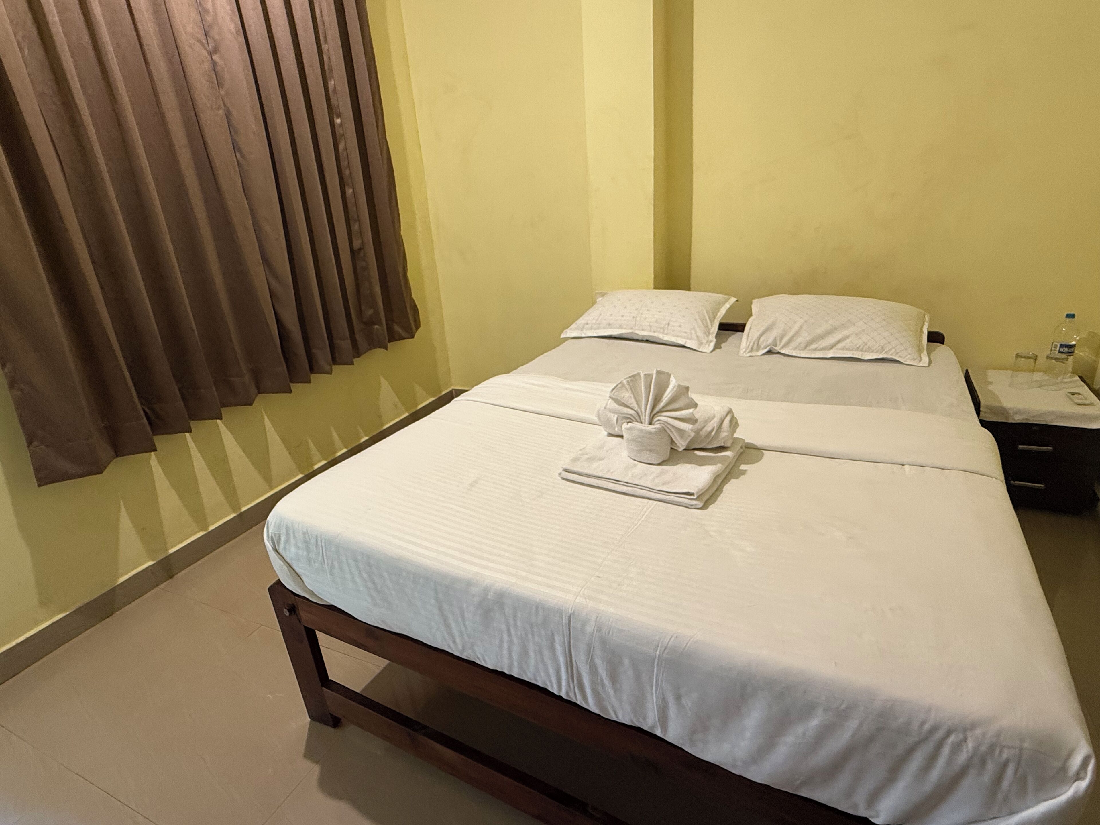 A hotel room with a bed, a nightstand, a bottle of water, and a towel on the bed.