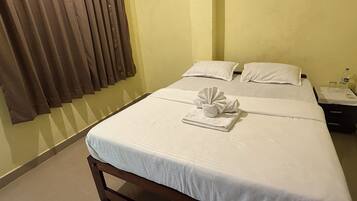A hotel room with a bed, a nightstand, a bottle of water, and a towel on the bed.