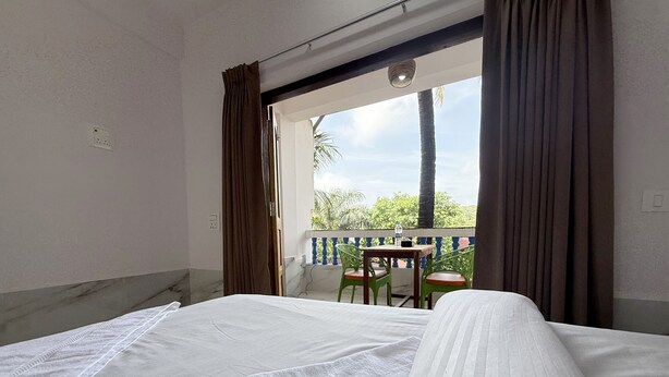Una habitación con una cama, un balcón con mesa y sillas, y vista a zonas verdes.