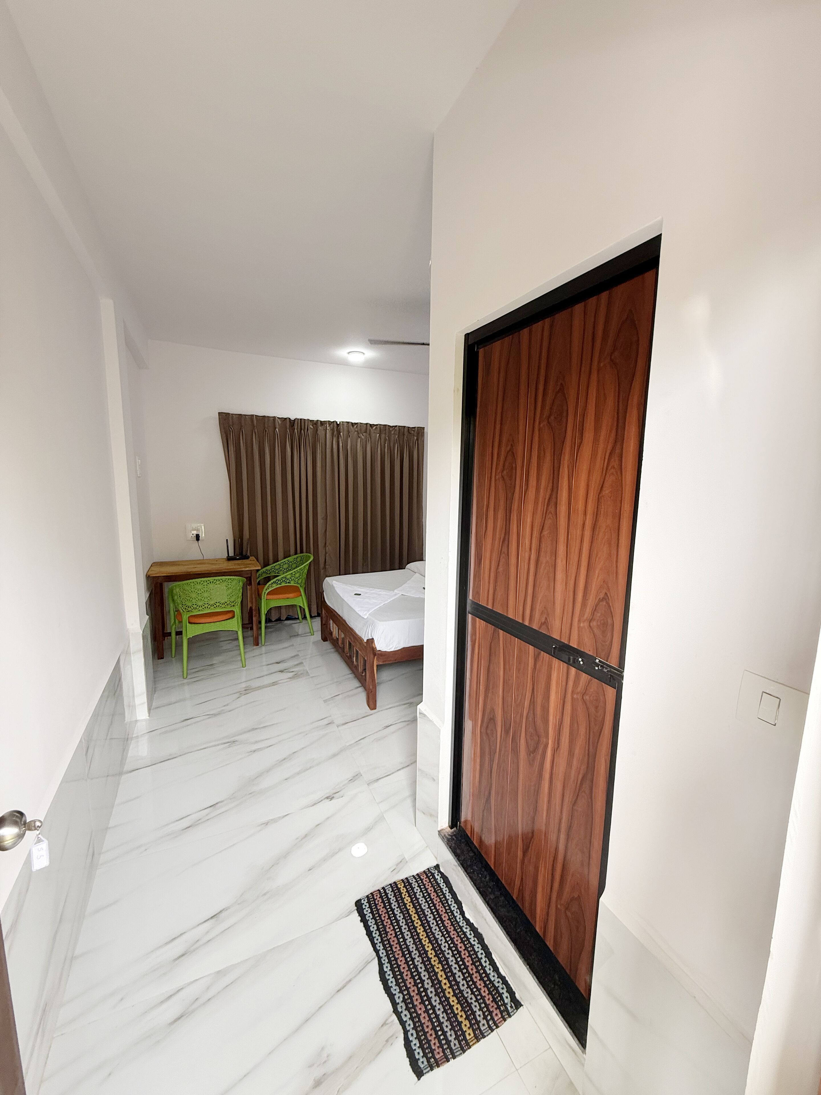 A room with a bed, a desk, two chairs, a wooden wardrobe, and a window with curtains.