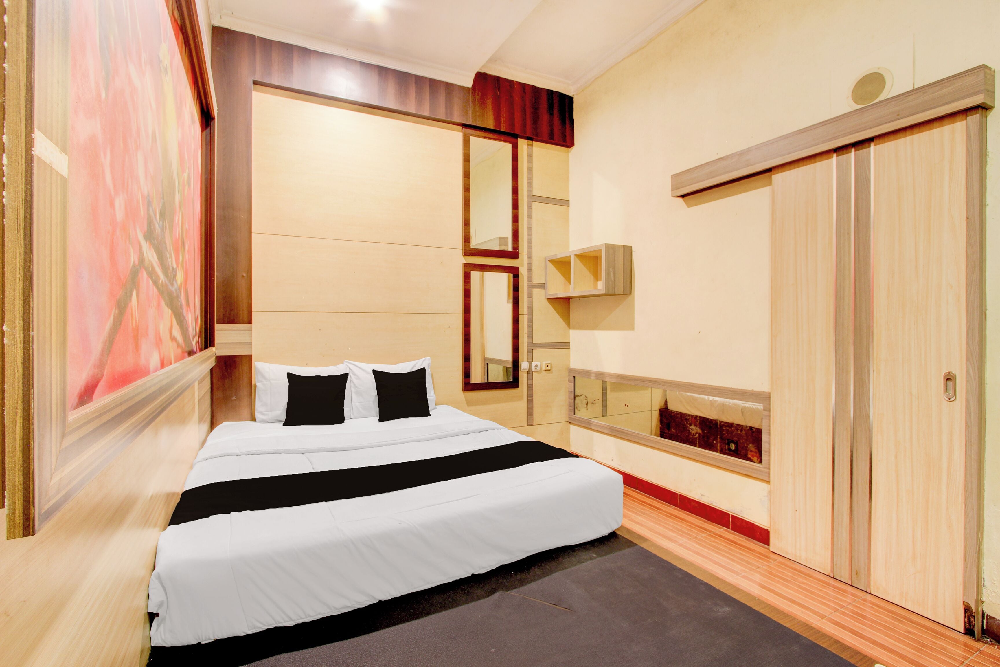 A hotel room with a large bed, a mirror, a wardrobe, and a painting on the wall.