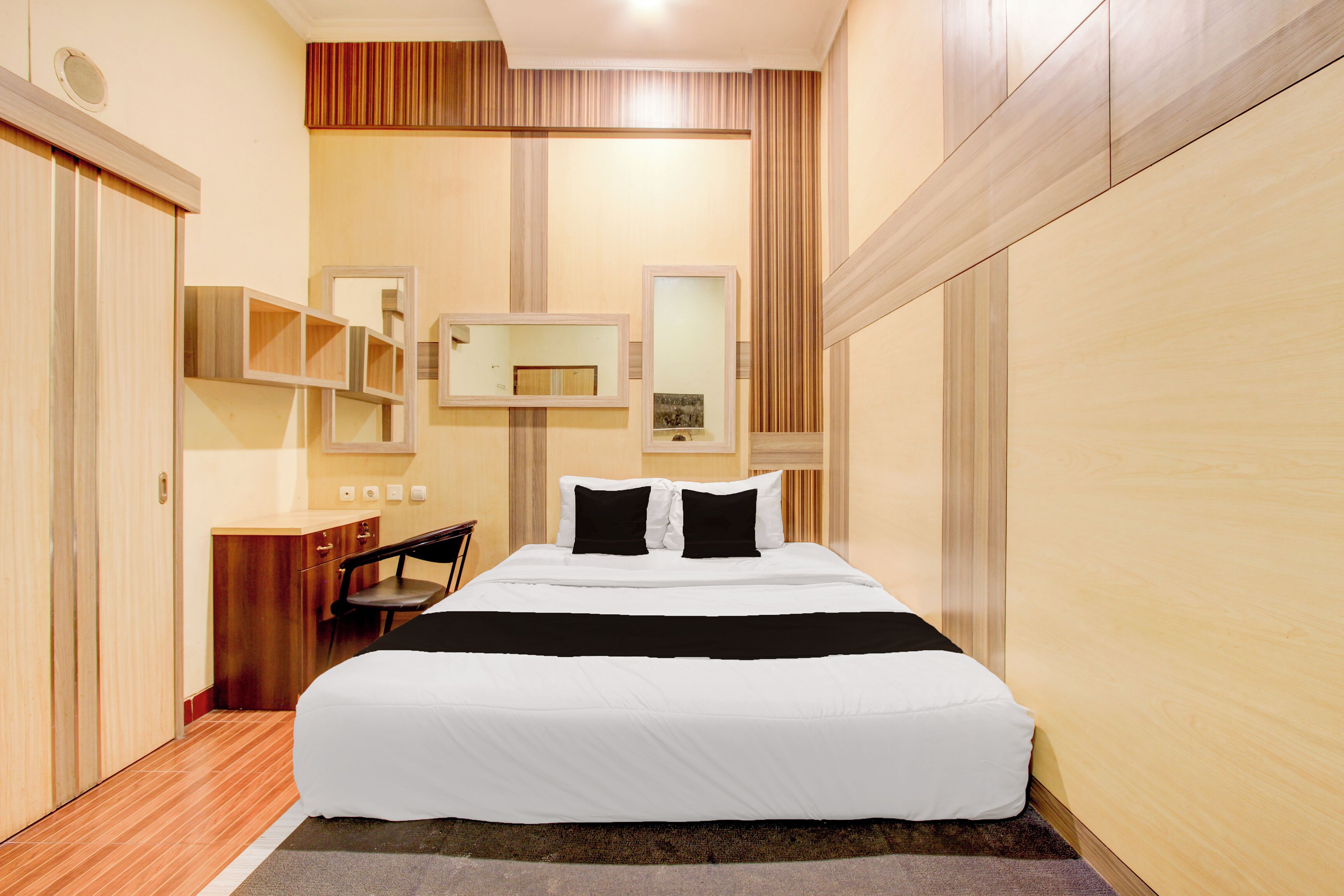 Ein Hotelzimmer mit einem großen Bett, einem Schreibtisch und einem Stuhl. Zwei Spiegel sind an der Wand angebracht und ein Kleiderschrank vorhanden.
