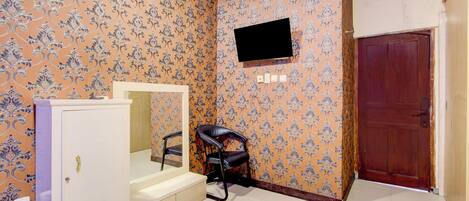 Una habitación con papel tapiz estampado, una puerta de madera, un televisor montado en la pared, un mueble espejo y una silla negra.