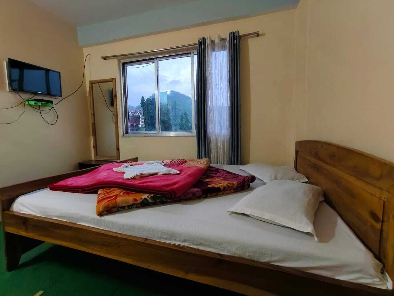 Habitación individual con una cama y cabecera de madera, ventana con cortinas, televisor de pantalla plana montado en la pared y alfombra verde.