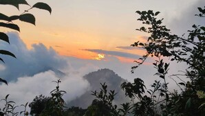 A mountainous landscape with a sunrise or sunset, clouds, and foliage. - Sherpa Residency (Kalimpong)