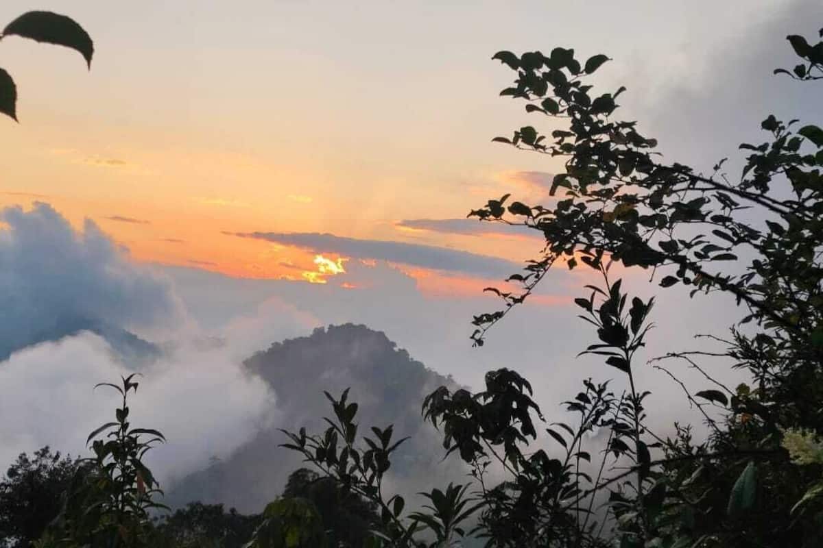Eine Berglandschaft mit Sonnenaufgang oder Sonnenuntergang, Wolken und Vegetation.