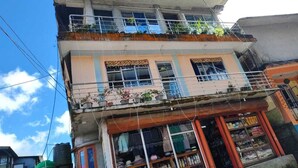 A multi-story building with balconies, a ground-level shop, and visible power lines. - Sherpa Residency (Kalimpong)