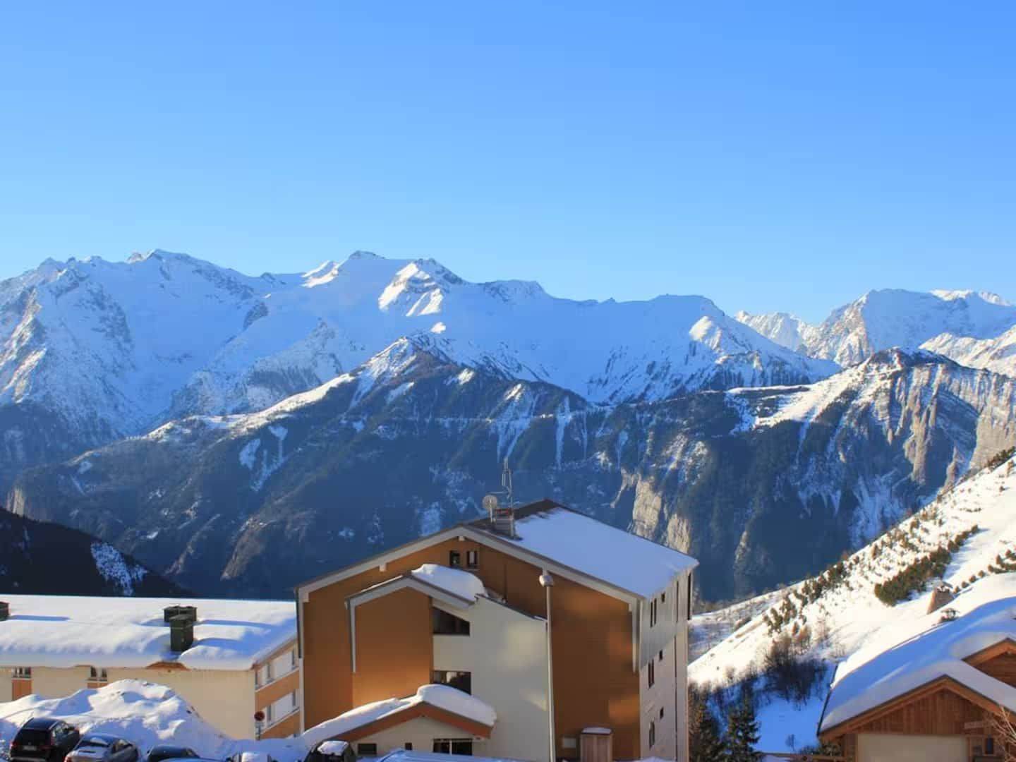 Une station de montagne où les bâtiments sont recouverts de neige et d’où l’on a une vue dégagée sur les sommets environnants.