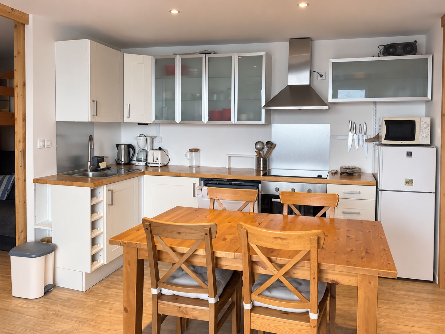 Una cocina compacta con armarios blancos, una mesa de comedor de madera y un lavavajillas empotrado.
