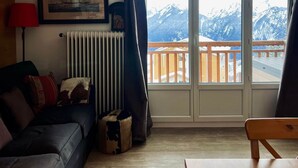 A living room with a couch, a table, a radiator, and a window with a mountain view. - Alpine Escape (Huez)