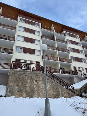 Un immeuble à plusieurs étages doté de balcons, d’un mur en pierre et d’un sol recouvert de neige.