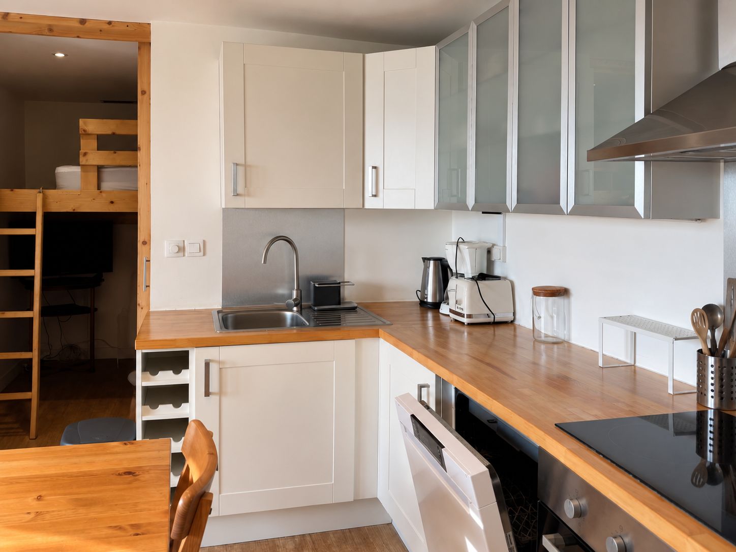 A modern kitchen with white cabinetry, a wooden countertop, a built-in dishwasher, and a stove.