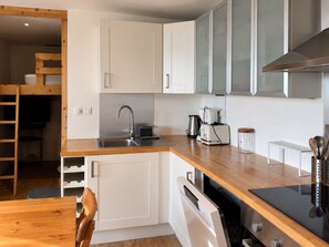 Ett modernt kök med vita skåp, en bänkskiva i trä, en inbyggd diskmaskin och en spis.