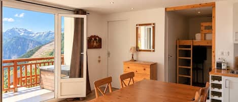 Una habitación con una mesa de comedor de madera, sillas, un aparador, un espejo y vistas a montañas a través de una puerta corrediza de vidrio.