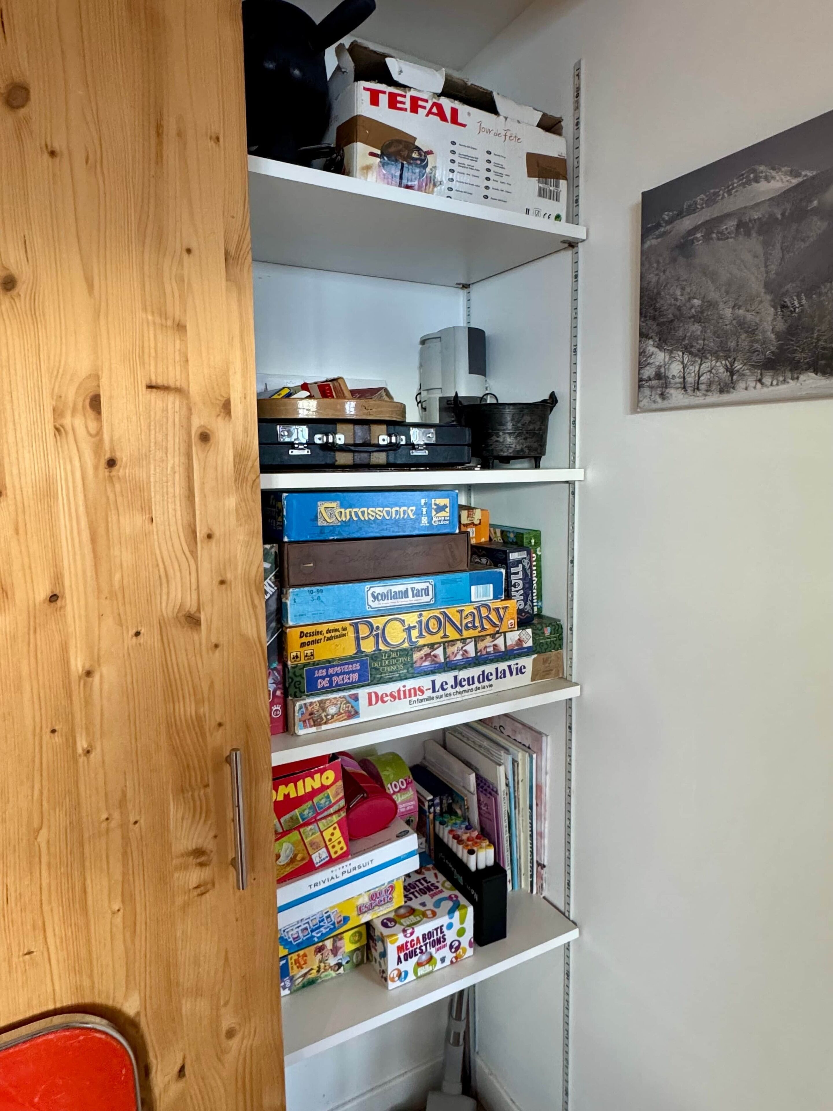 A bookshelf with various board games and a painting on the wall.