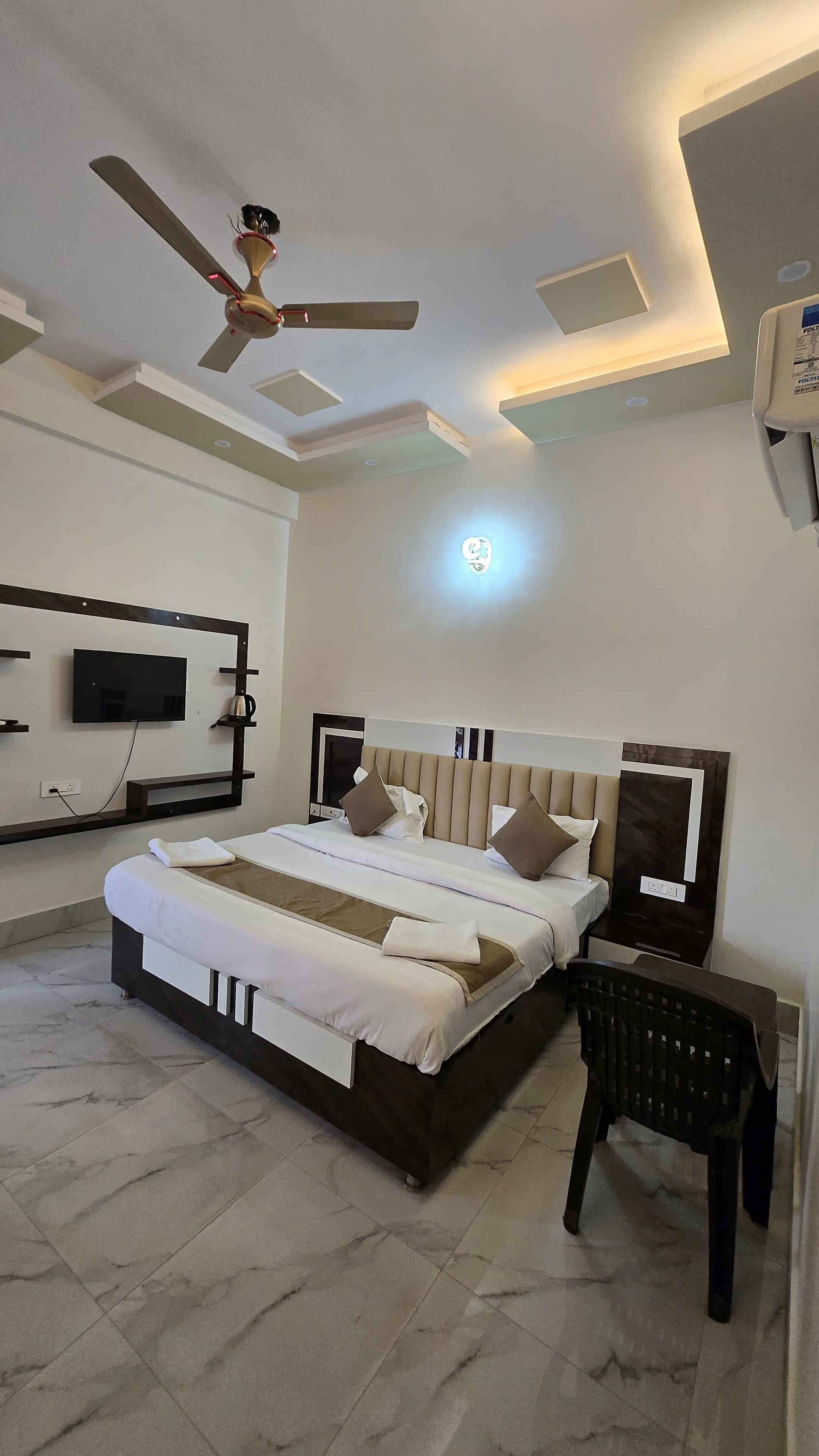 A modern hotel room with a large bed, a ceiling fan, a flat-screen TV, and a bedside table.