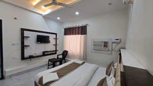 A modern hotel room with a flat-screen TV, a ceiling fan, an air conditioning unit, a massage table, and a window with curtains.