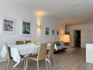A dining area with a white table, chairs, and a plate of fruit. There are framed pictures on the wall and a lamp in the background. - A two bedroom, sea view apartment in Skiper & Golf Resort Savudrija - Hortenzija (Crveni Vrh)