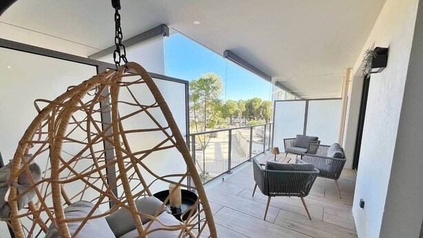Un balcón con una silla colgante, dos sofás y una mesa.