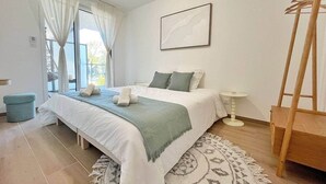 Un dormitorio con cama, mesita de noche, una silla y una ventana con cortinas.