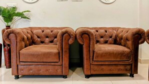 Two brown leather armchairs with tufted backs and armrests, positioned in front of a white wall with decorative wall art. - Crescent Stays Madhapur  (Hyderabad)
