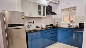 A modern kitchen with stainless steel appliances, blue cabinets, and a window. - Crescent Stays Madhapur  (Hyderabad)