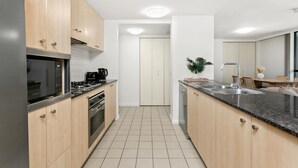 Eine moderne Küche mit Holzschränken, Edelstahlgeräten, einer schwarzen Arbeitsplatte und einem gefliesten Boden.
