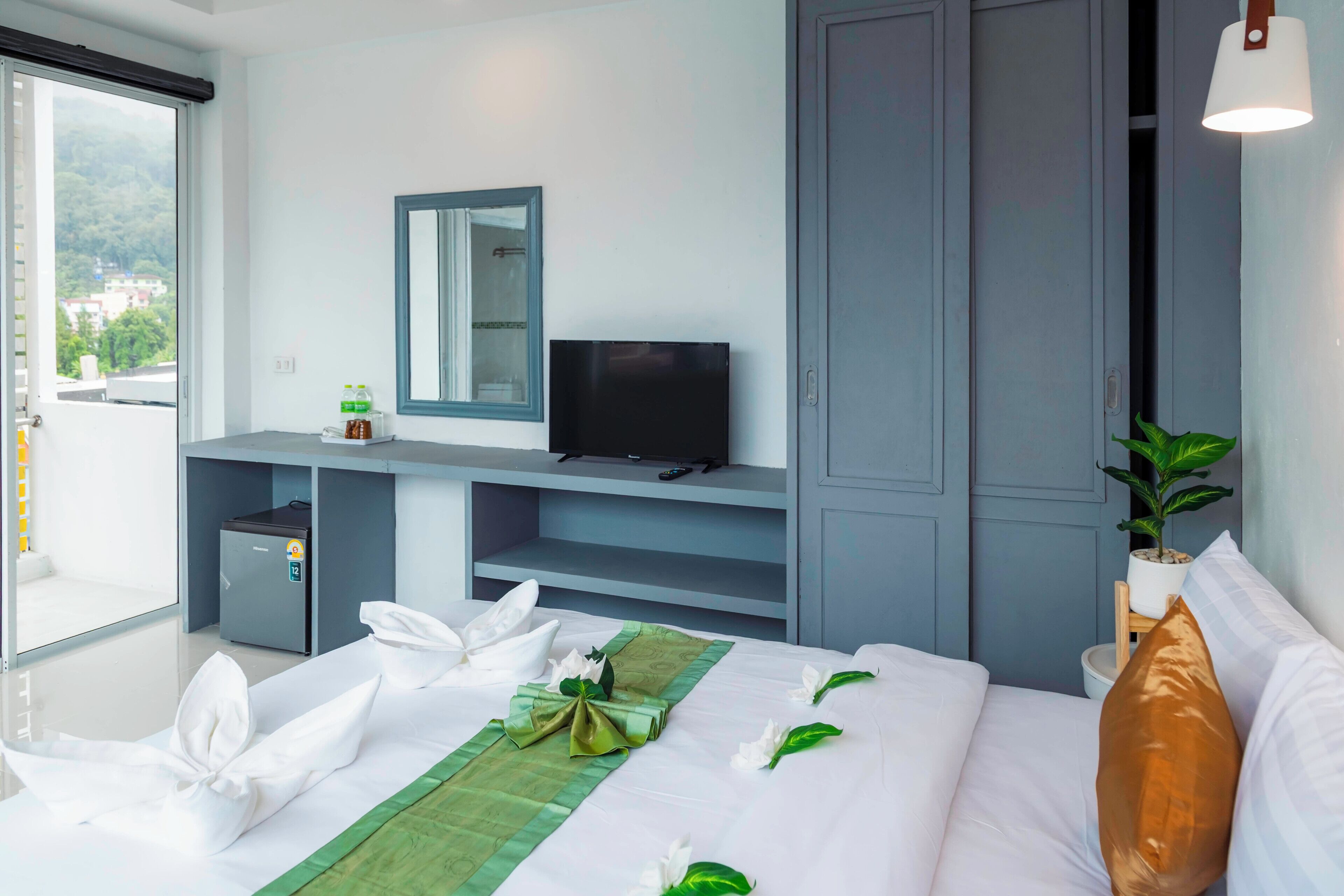 Une chambre d’hôtel équipée d’un lit, d’une télévision, d’un petit coffre-fort, d’une plante en pot et d’une porte coulissante donnant sur l’extérieur.