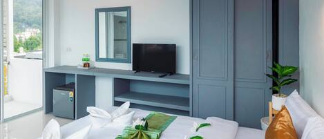 Une chambre d’hôtel équipée d’un lit, d’une télévision, d’un petit coffre-fort, d’une plante en pot et d’une porte coulissante donnant sur l’extérieur.